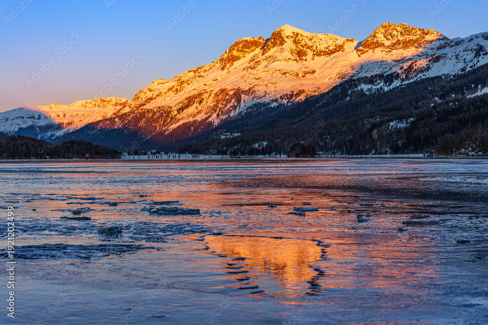 Obraz premium Sunset over the snow-covered mountain with color reflection on the frozen lake ice blocks on the Silsersee Lake in St. Moritz, Grisons, Switzerland