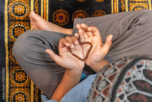 muslim boy with open hand lifted to pray and holding heart shaped prayer beads, ramadan religious concept