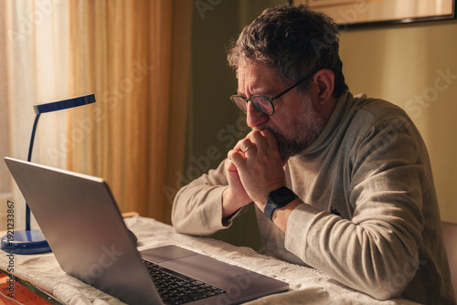 Schilderij op canvas Senior man reviewing financial information on laptop at home with concerned expr