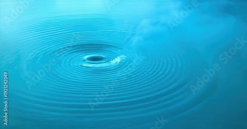 Water drop creates ripples. Blue tones dominate image. Calm surface disturbed by impact. Circular waves radiate outward. Peaceful scene.