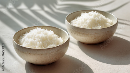 Two bowls of white rice on a table with shadows cast on it