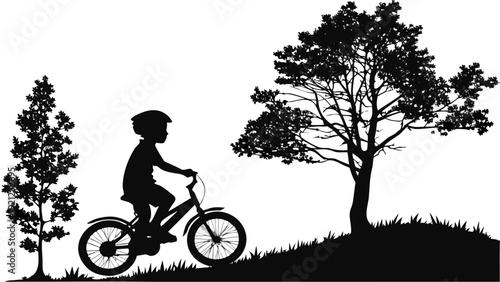 Silhouette of a young boy riding a bicycle on a grassy hill with trees.