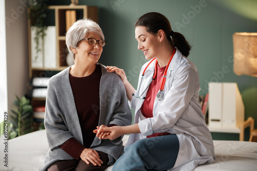 Schilderij op canvas Compassionate Female Doctor Comforting Senior Woman During Home Healthcare Visit