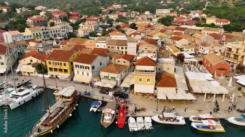 Top-Down Aerial View of the Vibrant Waterfront of Gaios, Paxos Island, Greece, Showcasing Terracotta Roofs, Bustling Cafes, Moored Boats, and Tourists Enjoying the Summer Atmosphere