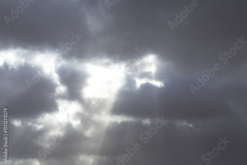 Soft sun rays break through dramatic clouds above the Lofoten fjords, illuminating islands, winter hills, and the rugged Arctic coastline under shifting northern light