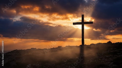 Sunbeams pierce dramatic clouds illuminating lone cross on hilltop at sunrise, religious symbol