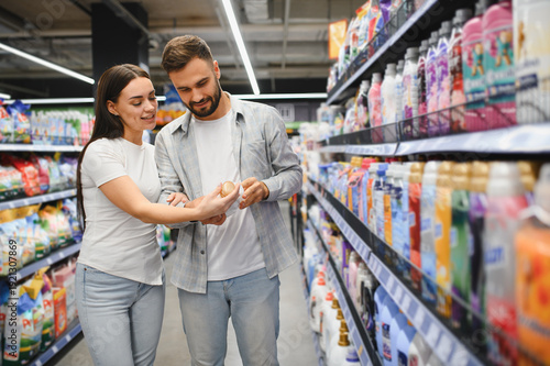 Quadro su tela Couple choosing laundry detergent in supermarket aisle
