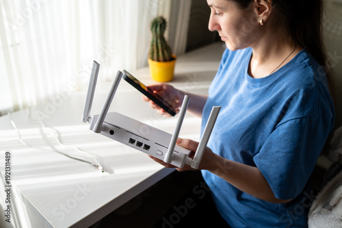 Bilde på lerret Woman Setting Up White Wi-Fi 6 Router with Smartphone in Bright Sunny Home Offic