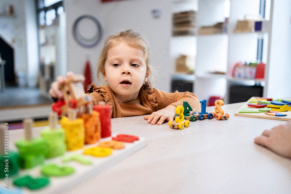 Fototapeta premium Preschool child learning numbers and developing motor skills with educational wooden toys at kindergarten, engaging in focused play during early childhood development activities