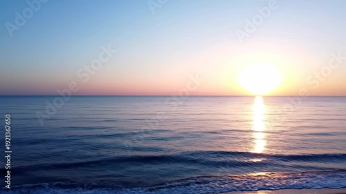 Tranquil ocean scene at sunrise, showcasing gentle waves and vibrant colors reflecting on the water's surface near the sandy shore