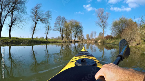 Quadro su tela A kayaker paddles through a serene, tree-lined river, capturing adventure and tranquility