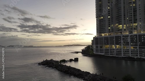 Cinematic aerial drone footage of the sunset over Cinta Costera in Panama City. The golden light of the sunset illuminates the coastal skyline, oceanfront boulevard, and modern buildings of the city, 