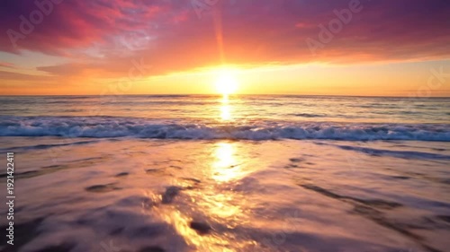 Serene ocean waves gently lap onto a sandy beach at sunset, casting a warm golden glow across the scene with vibrant pink and orange clouds.