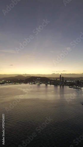 Cinematic aerial drone footage of the sunset over Cinta Costera in Panama City. The golden light of the sunset illuminates the coastal skyline, oceanfront boulevard, and modern buildings of the city, 