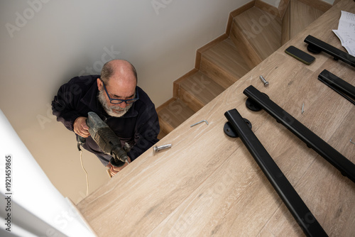 Man drilling into wood, installing a modern black handrail on stairs during home renovation