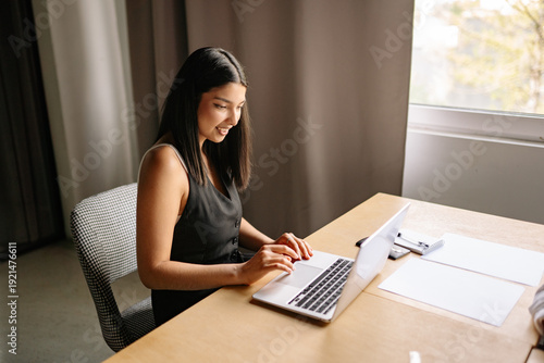 An Indian woman working diligently at her desk in a modern office, focusing on her laptop during a bright afternoon
