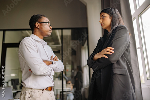 Two colleagues engaging in a serious discussion inside a modern office setting during daylight hours