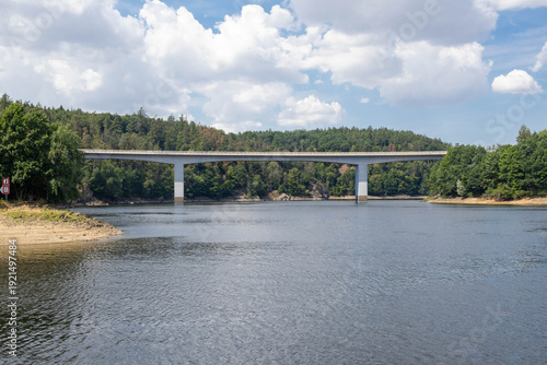 Concrete Road Bridge Over Dalesice Reservoir Surrounded by Dense Green Forest Under Blue Cloudy Sky
