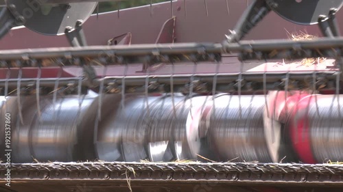 The harvest of grain. The threshing drum of the combine harvester close-up. A close-up of agricultural machinery with metal blades and green field background. 
