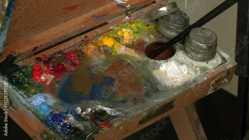 A close-up of an artists hand painting on canvas with a brush in a studio.  Art tools in the painter's atelier. Artist holding a brush and palette, he paints a picture