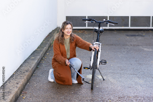 Woman inflating bicycle tire with pump on sunny urban alley