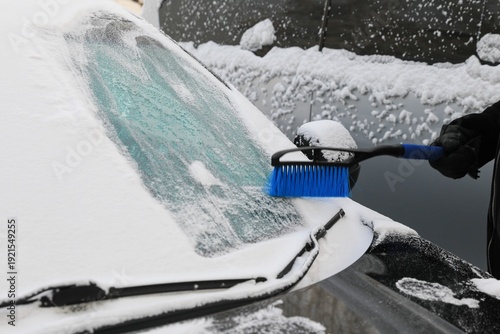 the driver clears snow and ice from the car's body after a snowstorm