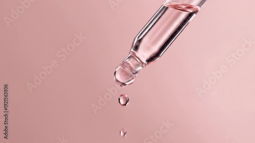 A mesmerizing close-up, macro shot captures a single, translucent drop of clear pink liquid detaching from the tip of a scientific glass dropper or pipette. The fluid glistens as it gracefully falls a