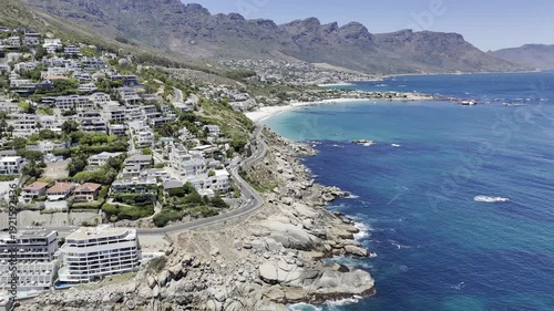 Drone orbits to the right at base of Lion's Head where it meets the sea in Sea Point and Clifton Beach on sunny day in Cape Town, South Africa