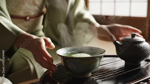 Green tea being poured from textured teapot into ceramic bowl wooden tray