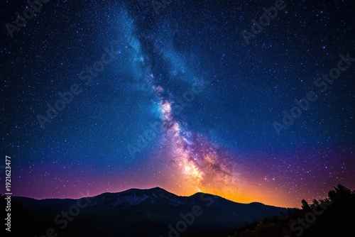 Silhouetted mountain ridge and trees beneath a vivid milky way and star-filled night sky with a glowing purple and orange horizon, evoking awe and wonder