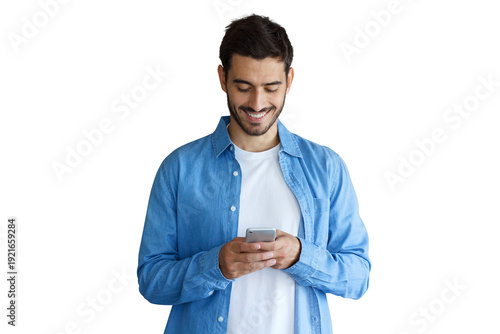 Happy young man in blue denim shirt texting on smartphone while smiling, looking down