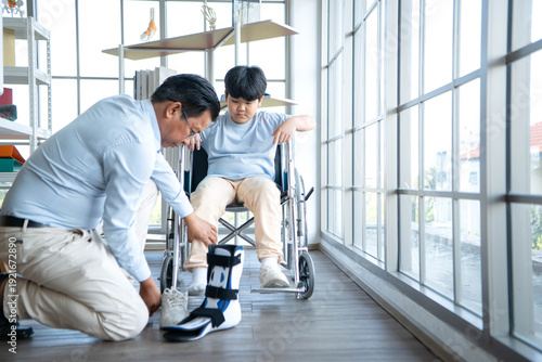 Wallpaper Mural Father adjusting orthopedic ankle brace for young boy in wheelchair, highlighting family support and rehabilitation care Torontodigital.ca