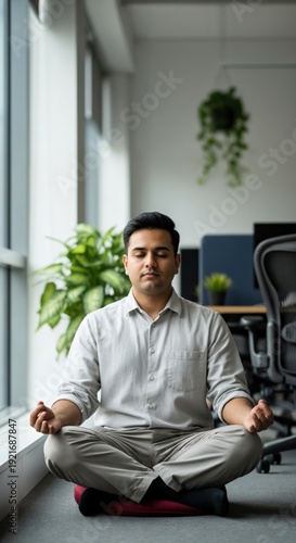 South Asian male professional practicing mindfulness meditation in modern office for mental health