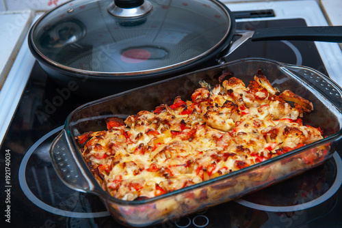 A Baked Vegetable Casserole of Cauliflower made with Potato, Sweet Bell Red Pepper, Chicken, Cheese and Tomatoes in Glass Baking Dish. Selective Focus.