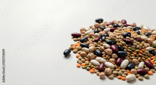 Mixed dry beans and lentils scattered in a loose pile in the lower right corner of a large off‑white surface, most of the background kept empty as negative space for nutrition or recipe text.