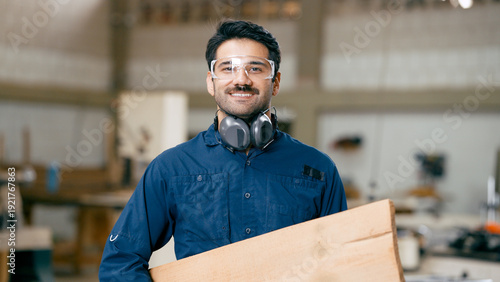 Slika na platnu Enthusiastic carpenter wearing safety goggles and ear defenders while holding wo