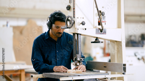 Cuadro en lienzo Woodworker operating a bandsaw to cut timber in a workshop while wearing protect