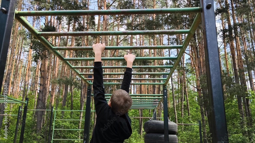 Obraz premium Young guy, Teenager, is playing sports on a horizontal bar on an outdoor playground. Boosts strength and endurance. sports on the horizontal bar. Rear view