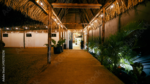 Schilderij op canvas Resort walkway illuminated at night, featuring a bamboo and thatch roof structur