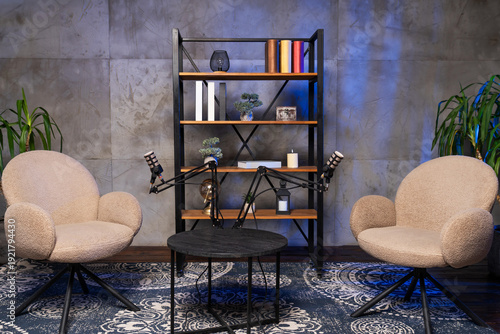 Podcast setup with two chairs, microphones, and a bookshelf in a simple room