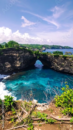 Scenic coastal rock arch frames turquoise ocean waters under a partly cloudy, blue sky. Nature's beauty