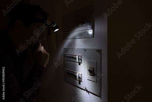 During a power outage a man with a headlamp examines his electrical panel.