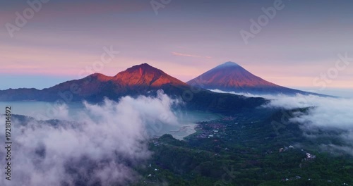 Volcanic landscape with Mount Batur and Mount Agung prominent above the clouds, capturing the calm beauty of the sunrise over Lake Batur and surrounding villages in Bali, Indonesia. Aerial view flight