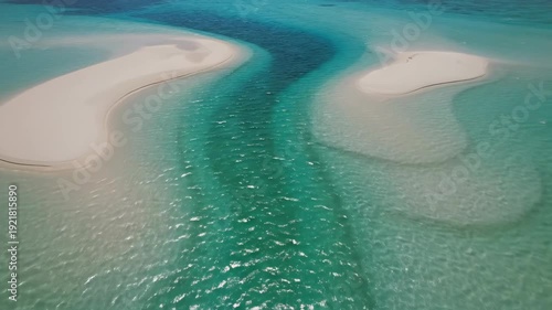Aerial view of turquoise water flowing between two sandy islands, showcasing the gradual transition of colors and textures in a tropical coastal landscape