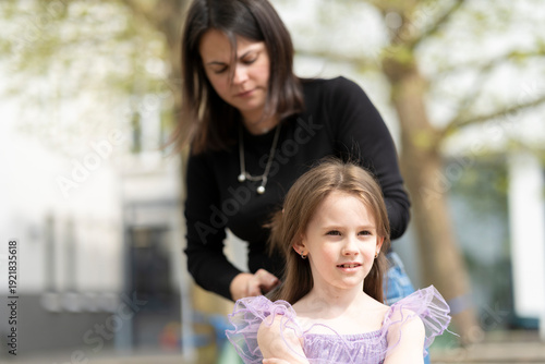 Mother and daughter in a carnival costume scene, beautiful smiling girl standing beside her mom. Concept of family love, childhood happiness and festive preparation.