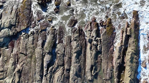 Waves wash over rocks as people explore the shoreline during low tide. The sun shines brightly in the coastal area.