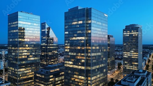 Stunning Aerial View of Modern City Skyscrapers at Dusk with Illuminated Windows and Blue Sky.