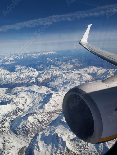 Photo of a beautiful landscape of the snow-capped Alps mountains in Italy from the window of a flying airplane with a view of the wing and turbine.