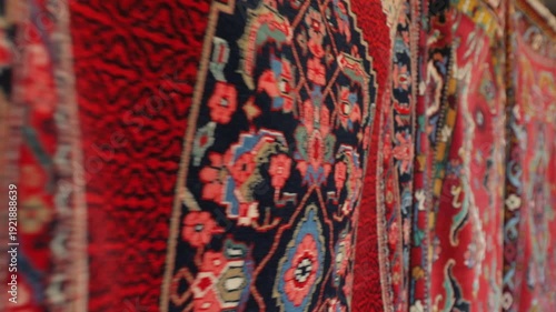 Slow pan close-up shows traditional hand-woven rugs. Vibrant colors and intricate patterns. Ideal for textile crafts, oriental design, cultural heritage, and market atmosphere.