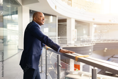 Fényképezés Confident mature black businessman standing in modern office atrium, leaning on